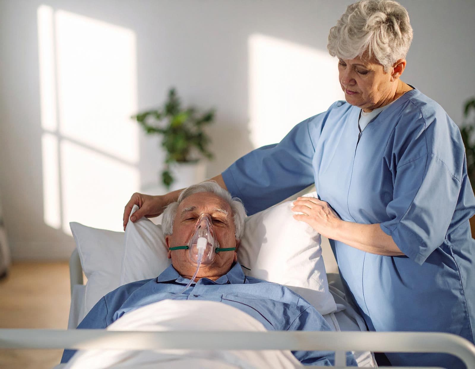 Pflegekraft richtet Kissen unter dem Kopf eines älteren Patienten im Bett