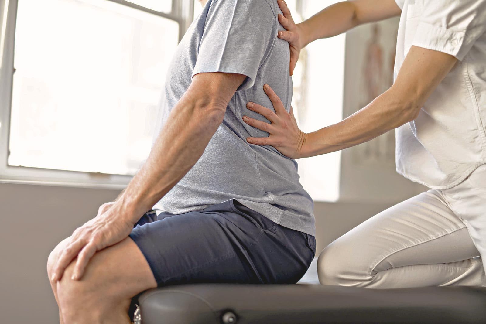 Physiotherapeut tastet den Rücken eines sitzenden Mannes ab