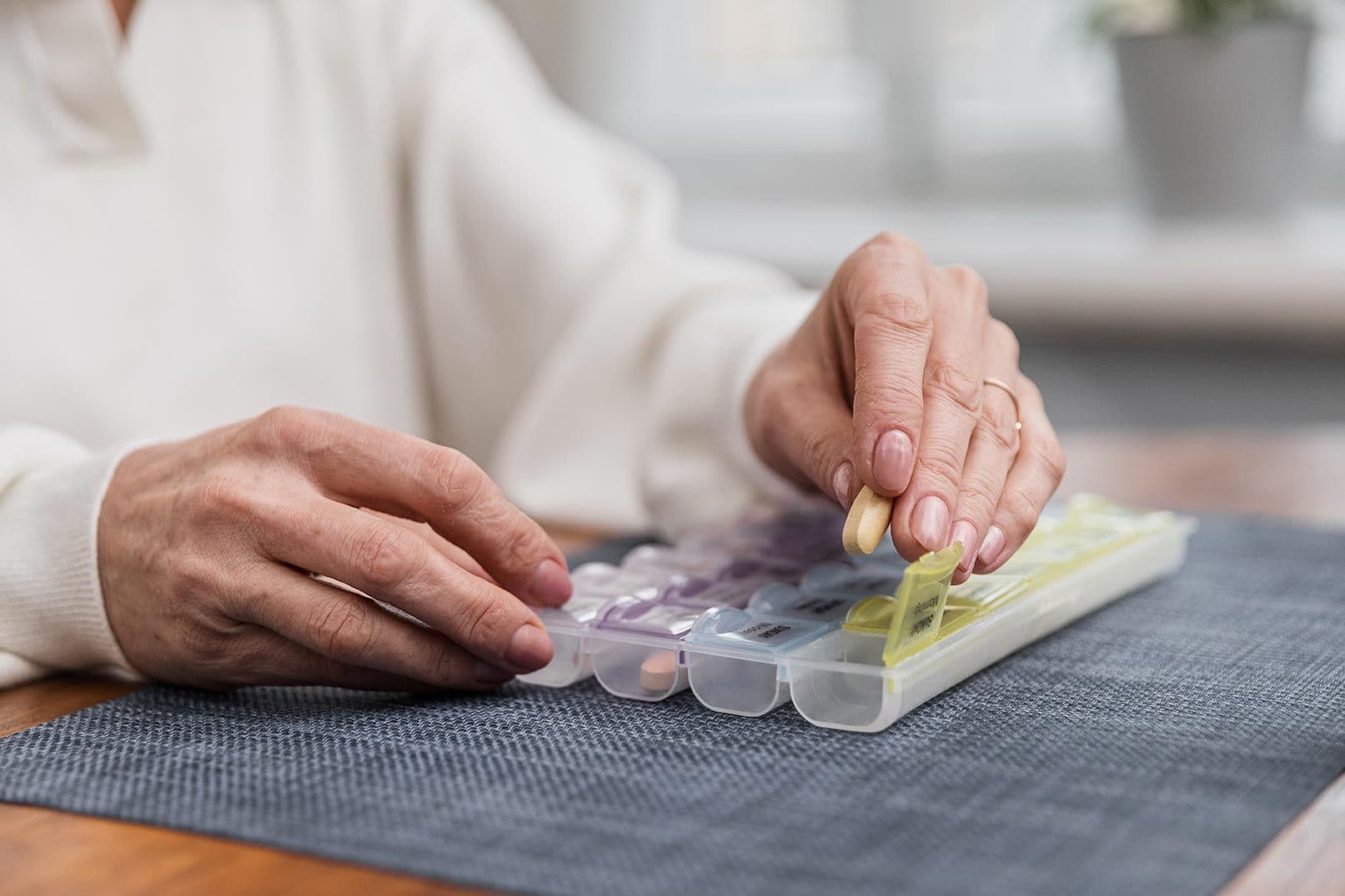 Seniorin legt Tabletten in ein wöchentliches Medikamenten-Organizer mit Fächern