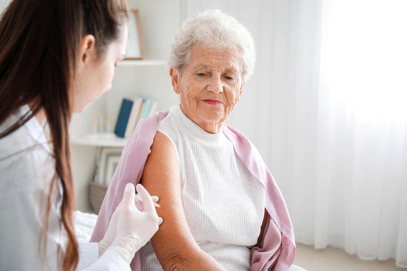 Seniorin erhält von Arzt eine Injektion in den Oberarm