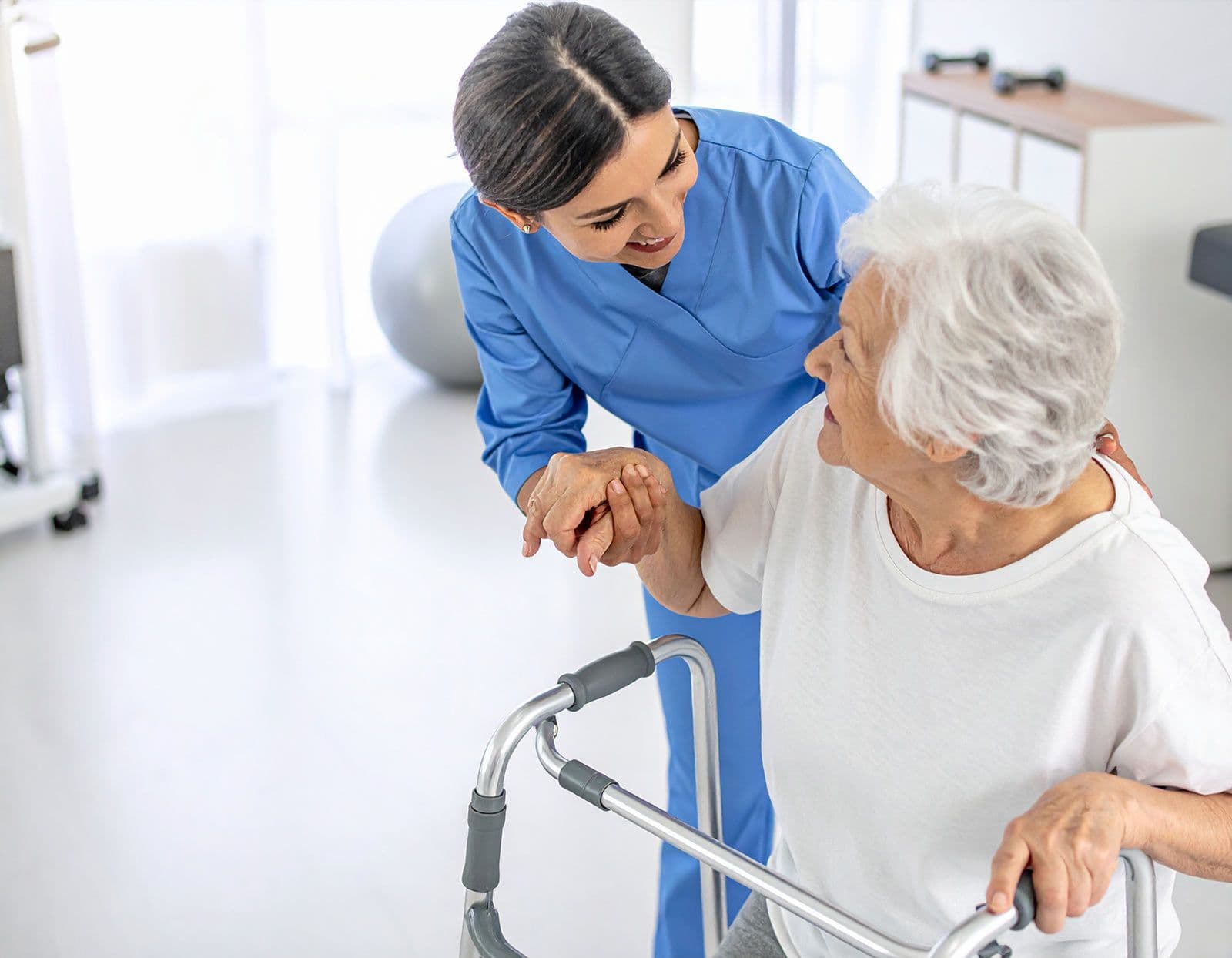 Seniorin benutzt einen Rollator, wird von einer Pflegekraft während einer Physiotherapie unterstützt