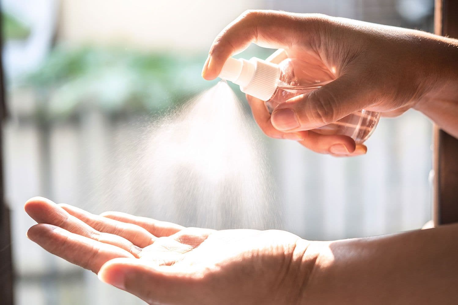 Person sprüht mit einer Hand Desinfektionsmittel auf die andere Hand