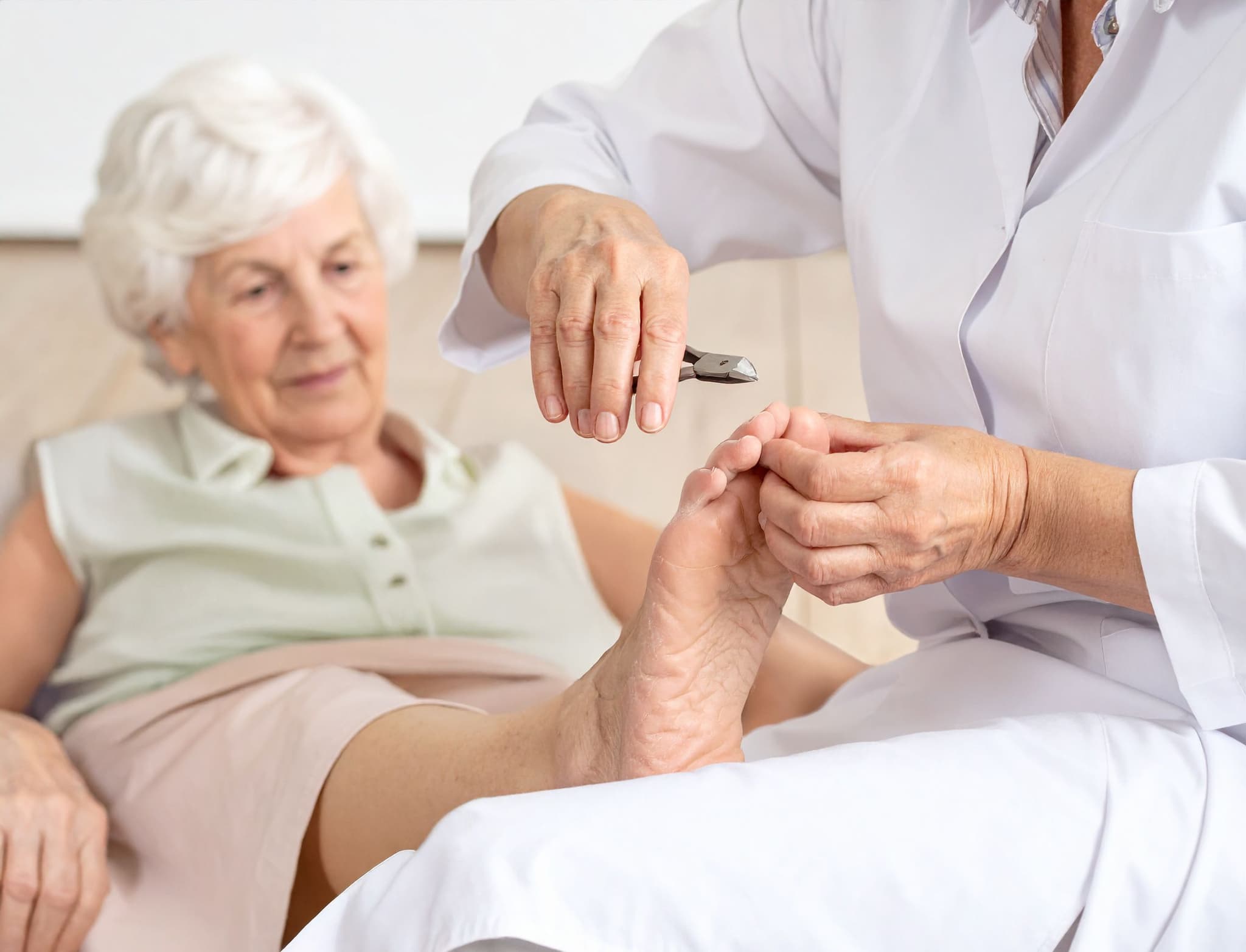 Pflegekraft schneidet die Fußnägel einer älteren Frau mit einer Nagelzange