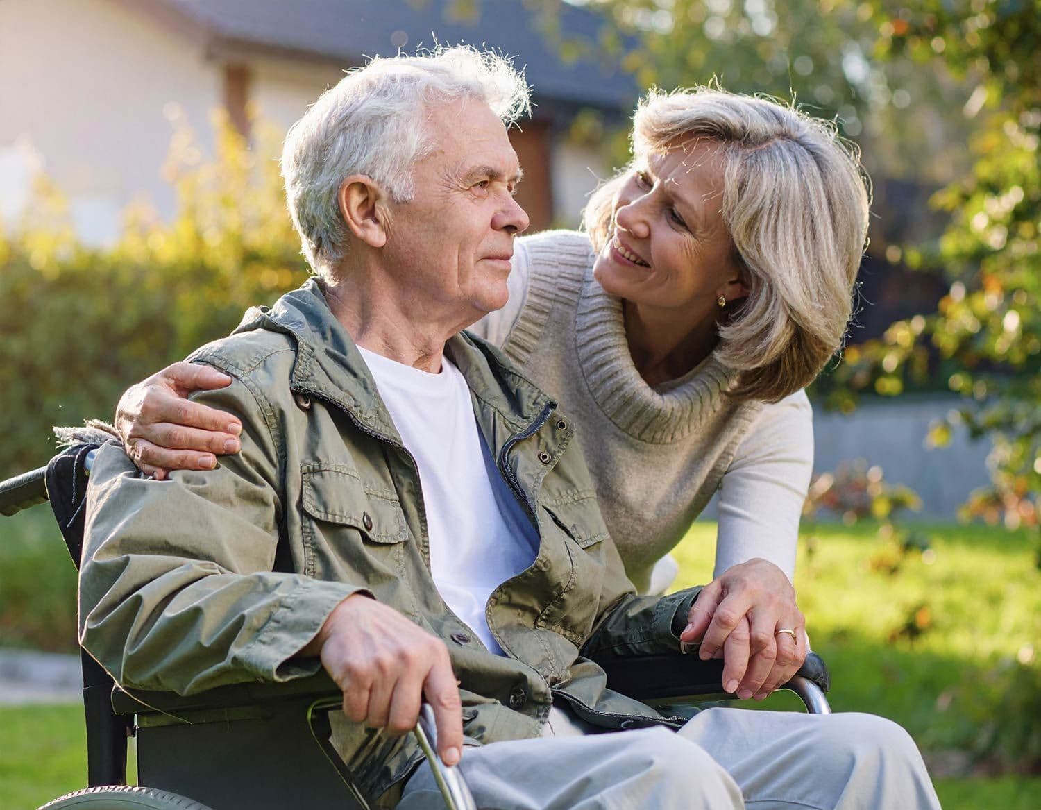 Älterer Mann im Rollstuhl, wird von Frau umarmt