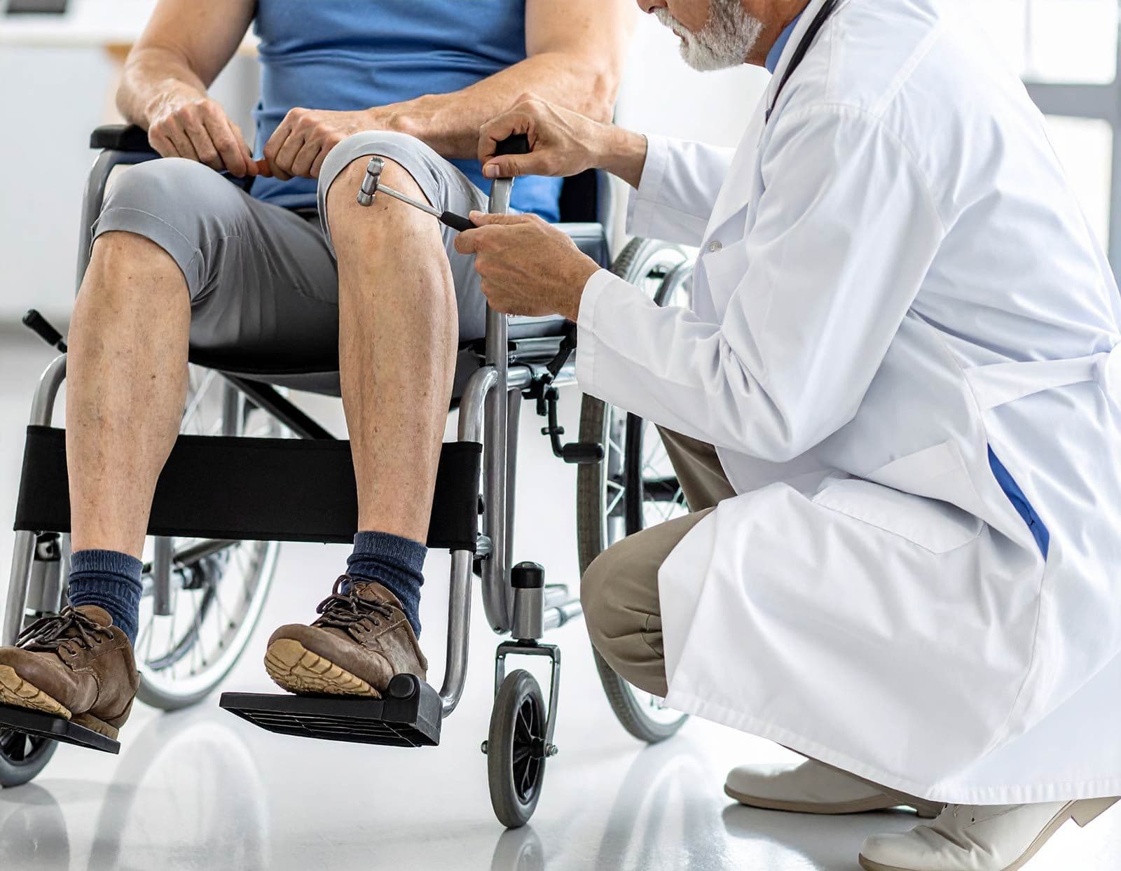 Älterer Mann im Rollstuhl, Arzt misst mit Reflexhammer sein Knie