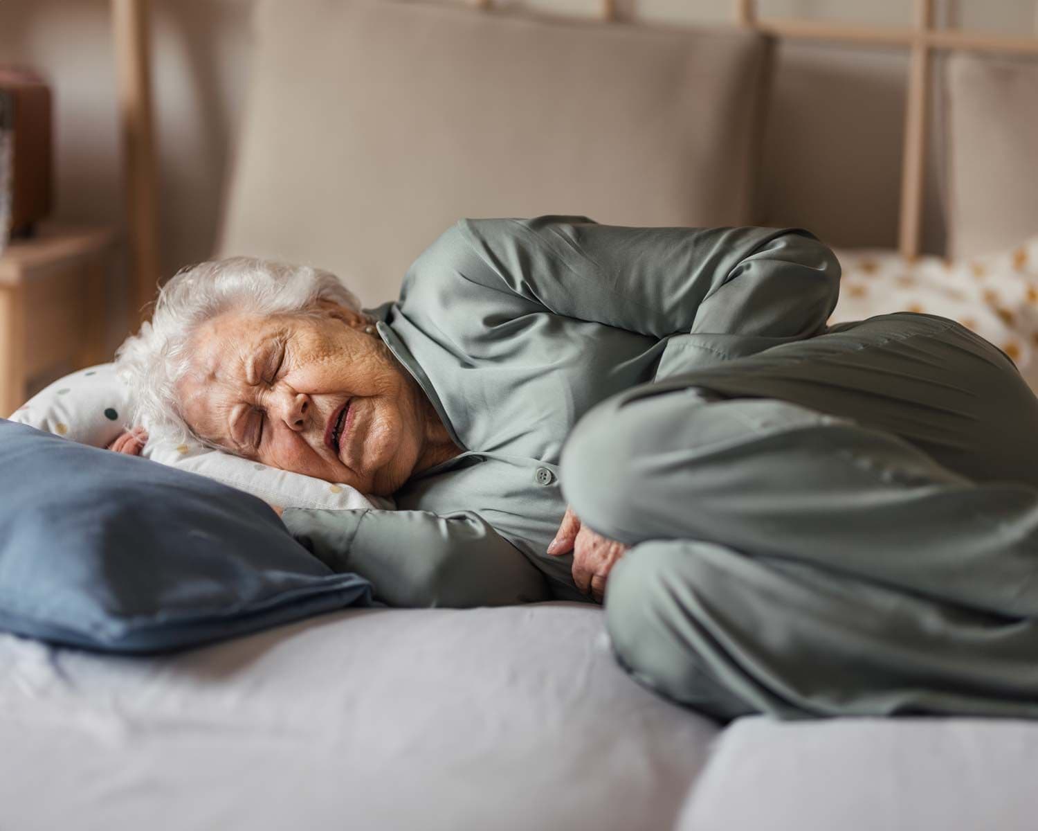 Ältere Frau liegt auf der Seite im Bett und hält ihren Bauch