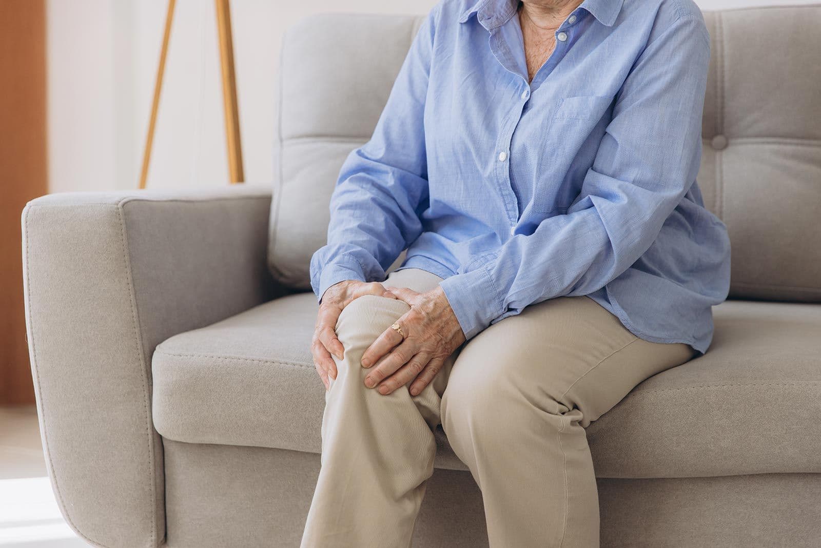 Ältere Person sitzt auf Sofa und hält schmerzhaft ihr Knie