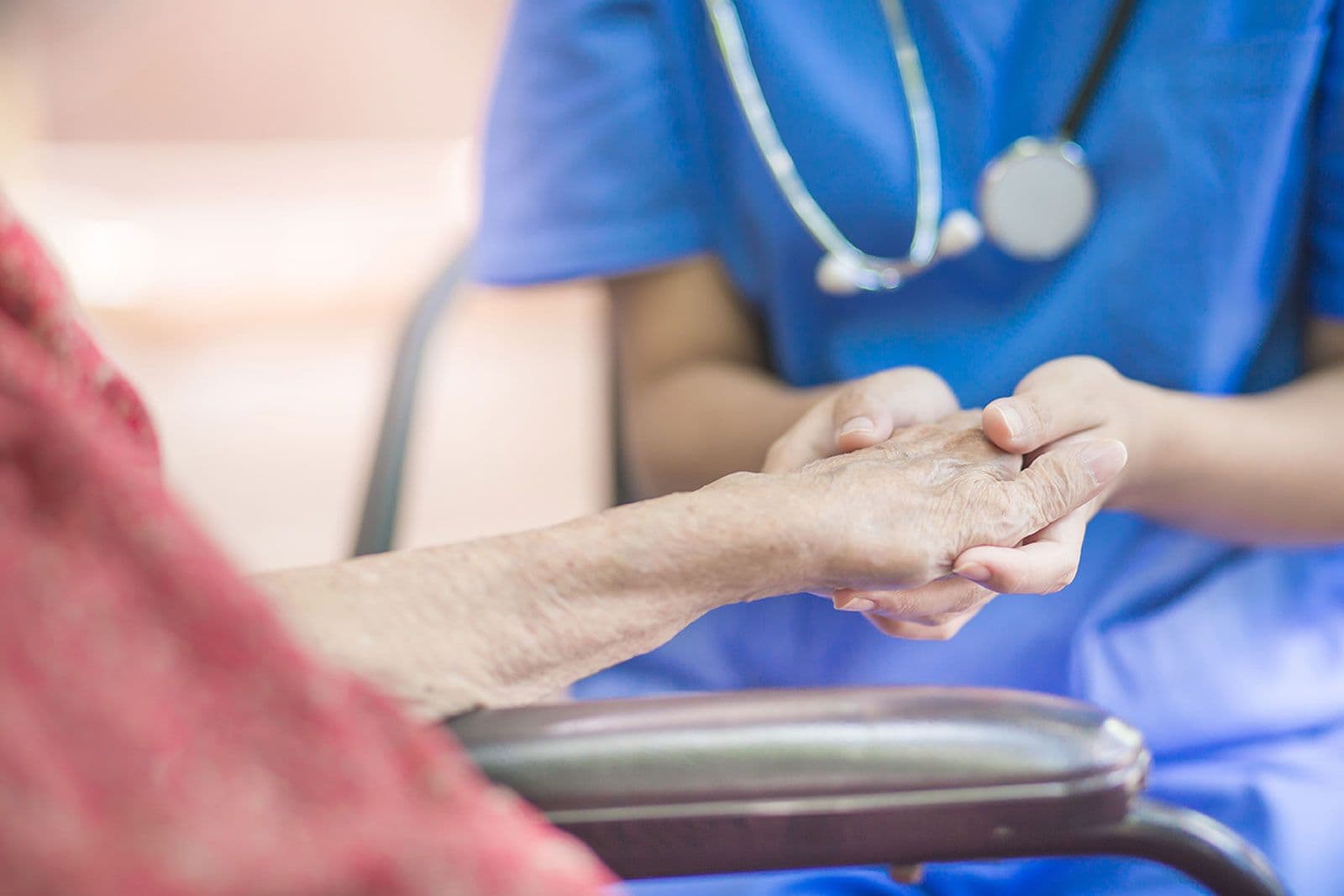 Pflegekraft hält die Hand einer älteren Person im Rollstuhl