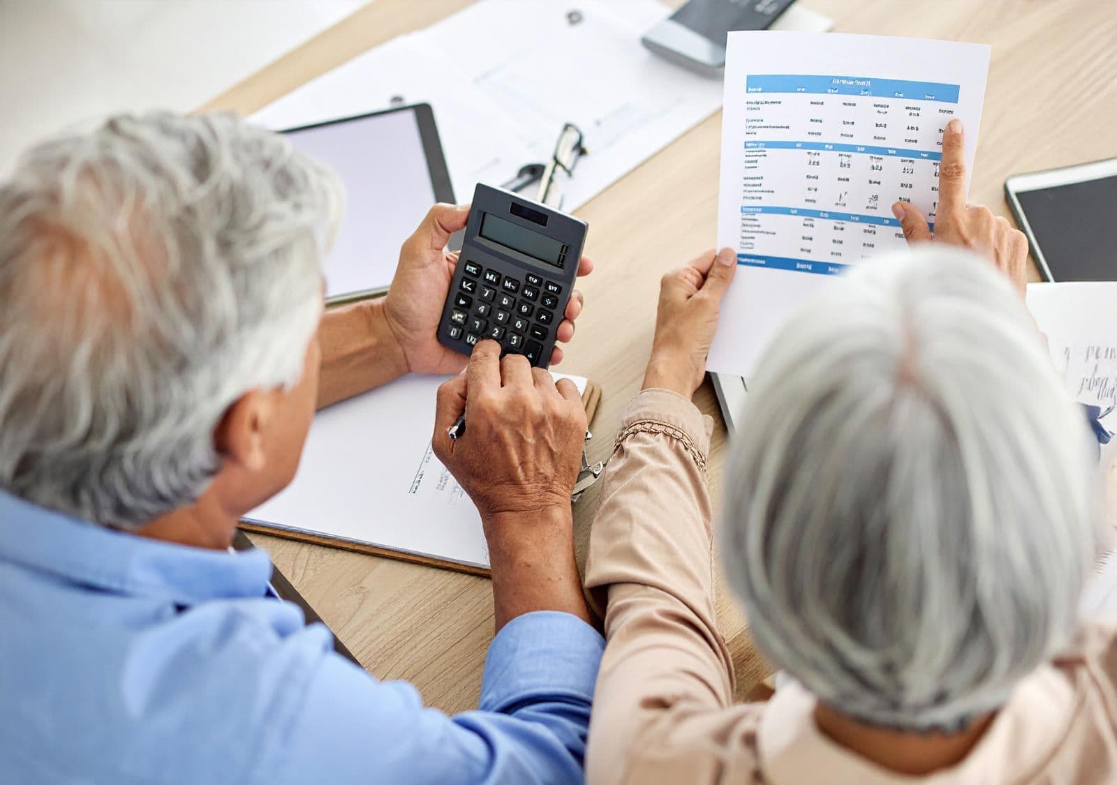Älteres Paar sitzt am Tisch und prüft gemeinsam Unterlagen mit Taschenrechner