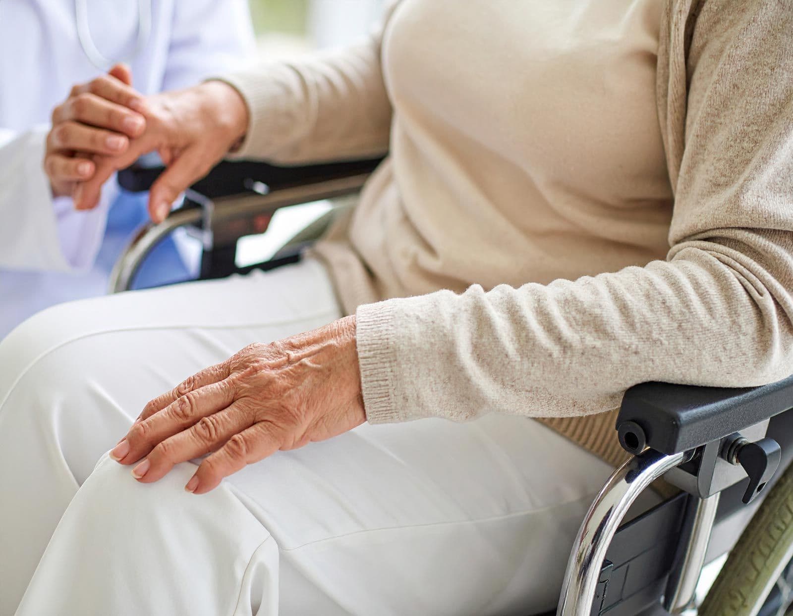 Pflegekraft hält die Hand einer älteren Person im Rollstuhl