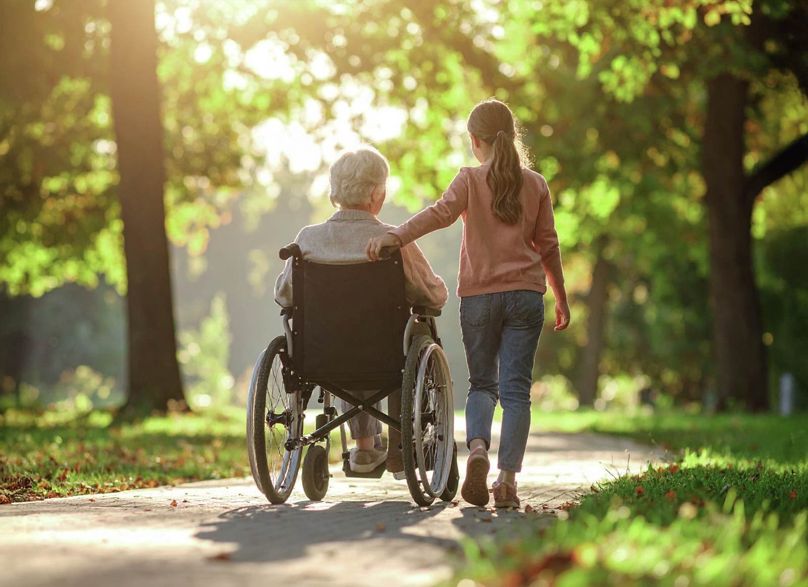 Mädchen schiebt ältere Frau im Rollstuhl auf einem Weg im Park