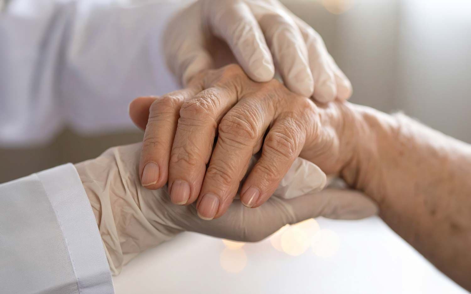 Pflegekraft hält behutsam die von rheumatoider Arthritis betroffene Hand einer älteren Frau
