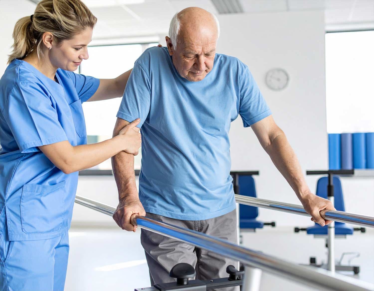 Älterer Mann erhält Physiotherapie nach Schlaganfall, stützt sich auf Parallelbarren, begleitet von Therapeutin in Klinik