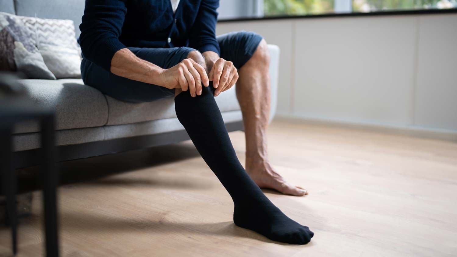 Mann sitzt auf Sofa und zieht schwarzen Kompressionsstrumpf an