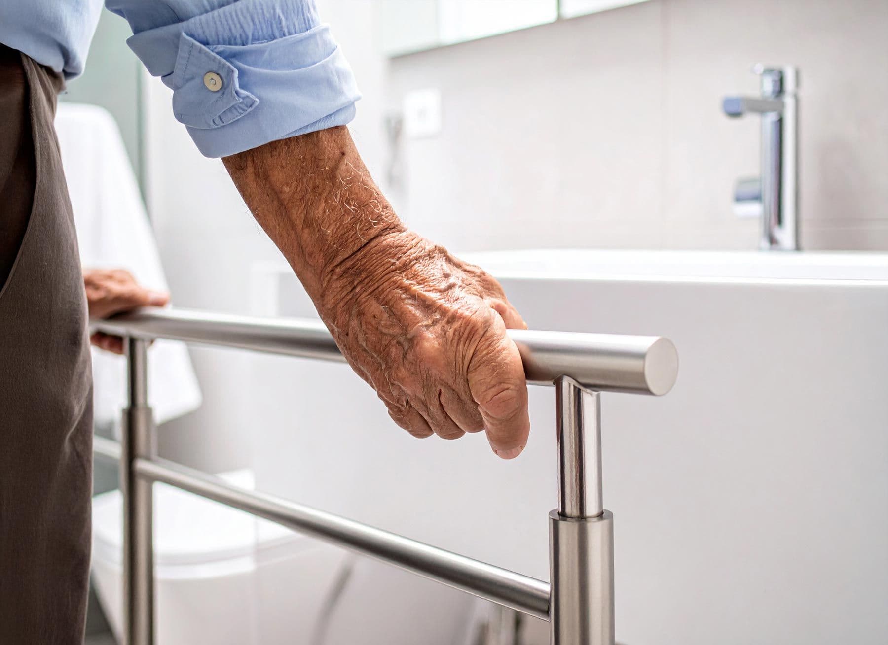 Hand eines älteren Menschen hält sich an einem Haltegriff im Badezimmer fest