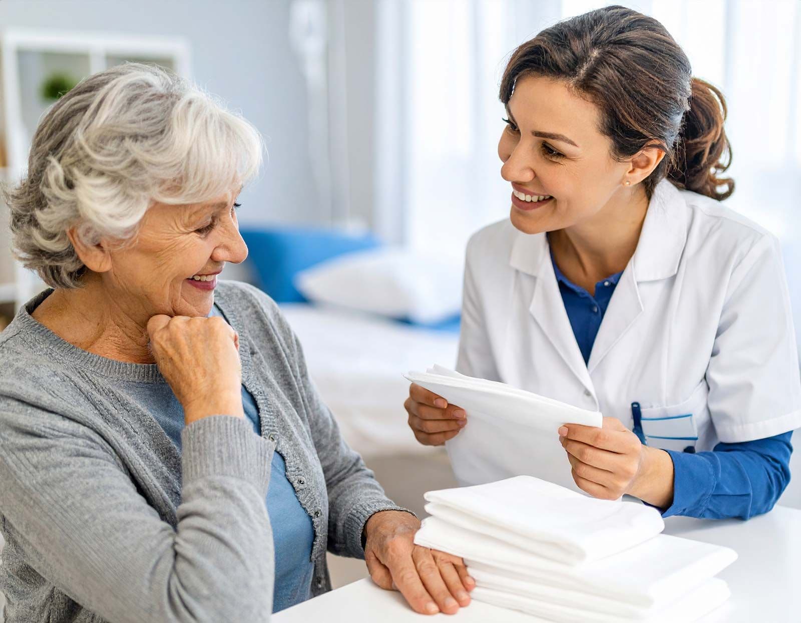 Pflegekraft überreicht einer Seniorin Schutzunterlagen