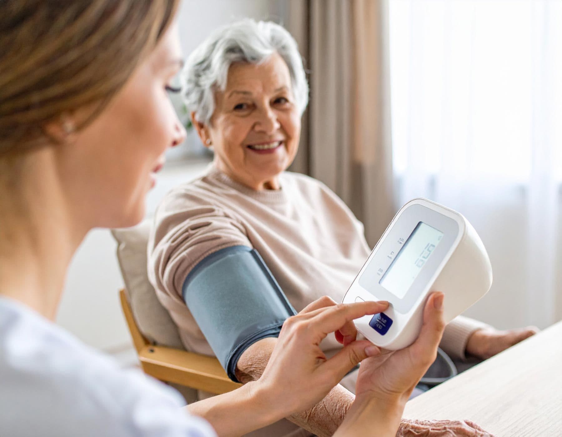 Pflegekraft misst Blutdruck einer älteren Frau mit Blutdruckmessgerät am Oberarm
