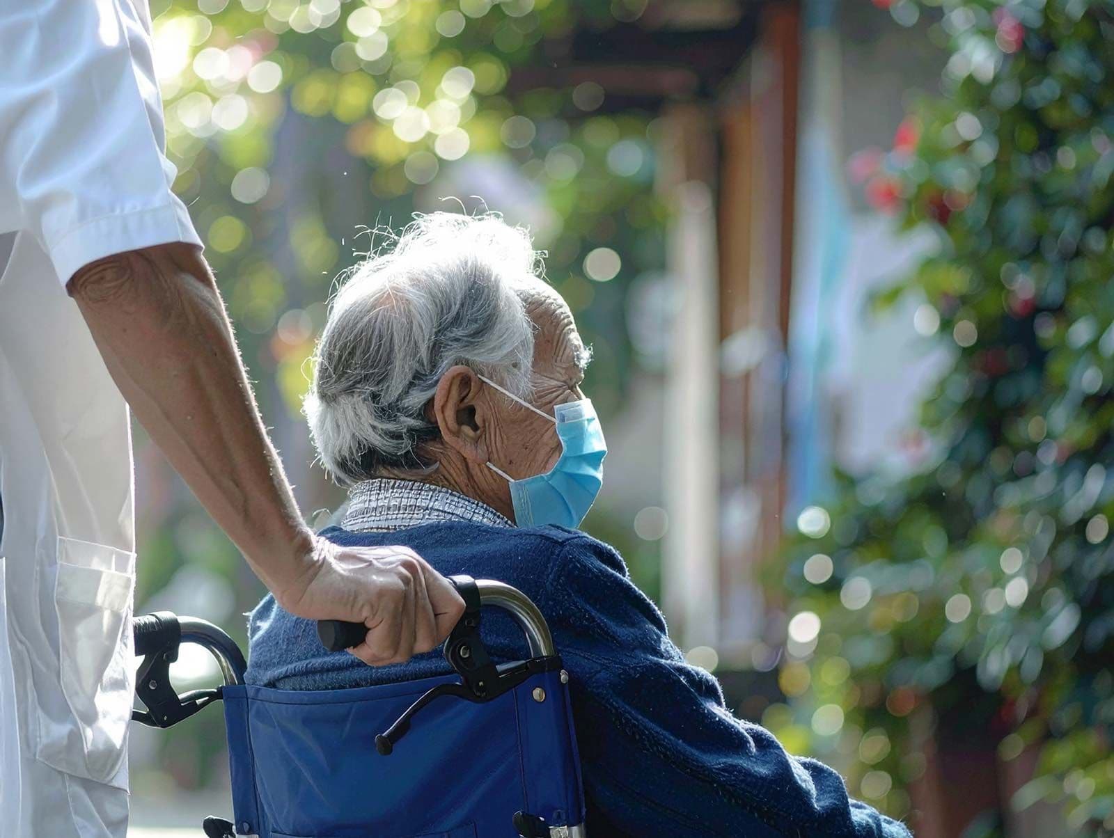 Senior im Rollstuhl, der eine medizinische Maske trägt
