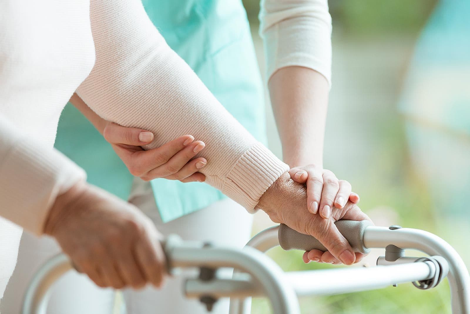 Pflegekraft hält unterstützend den Arm einer älteren Person, die einen Rollator benutzt