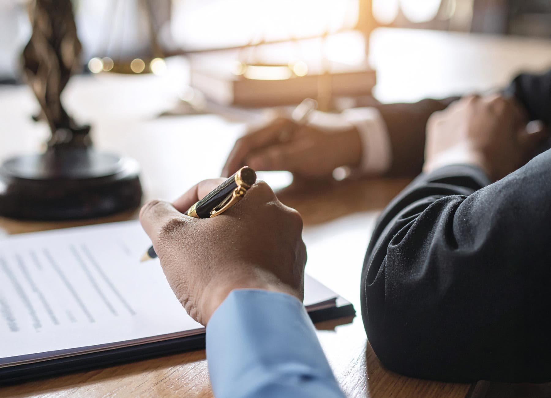 Person unterschreibt juristische Dokumente auf einem Schreibtisch