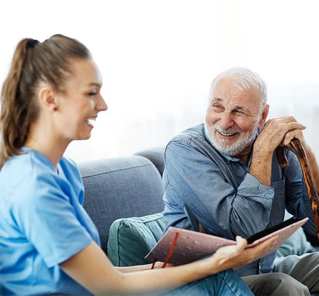 Pflegekraft sitzt mit einem älteren Pflegebedürftigen